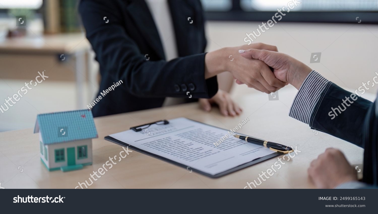 stock-photo-real-estate-agent-shaking-hands-with-client-over-contract-in-office-setting-with-model-house-and-2499165143